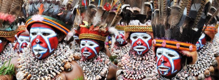 Close up of a female group at the SingSing festival- they have red and white facepaint, huge shell necklaces and enormous feathered headdresses, PNG