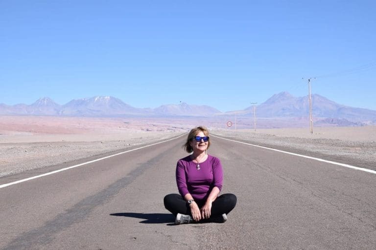 Sue sitting in the centre of a deserted road leading across the Atacama Desert to the Andes, Chile