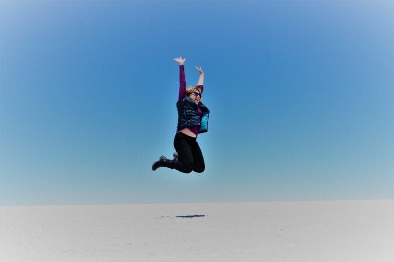 Sue leaps into the blue sky above the snow white salt flats at Salar de Uyuni